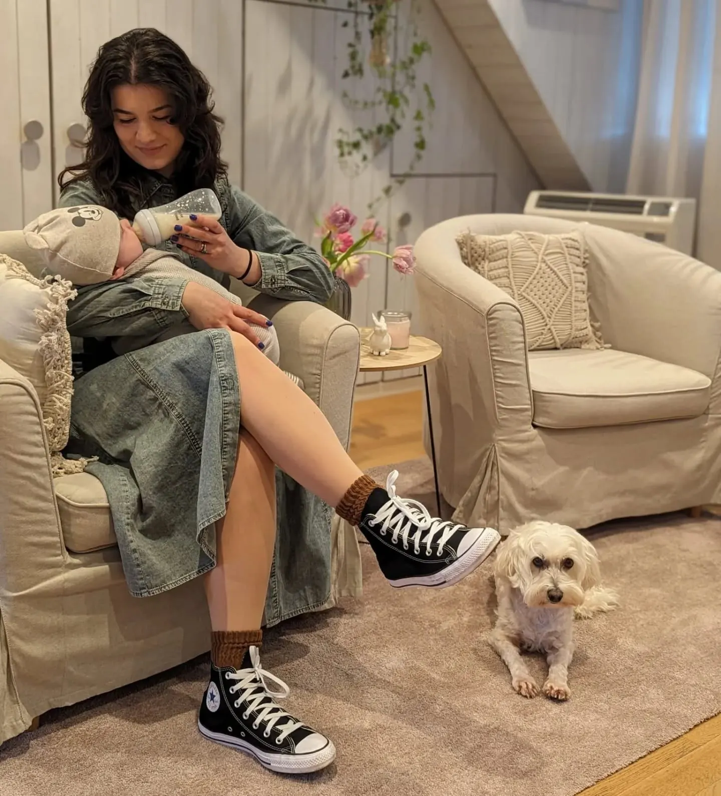 Denisa im Sessel ihres Studios mit einem Baby im Arm, Shyva liegt davor auf dem Teppich