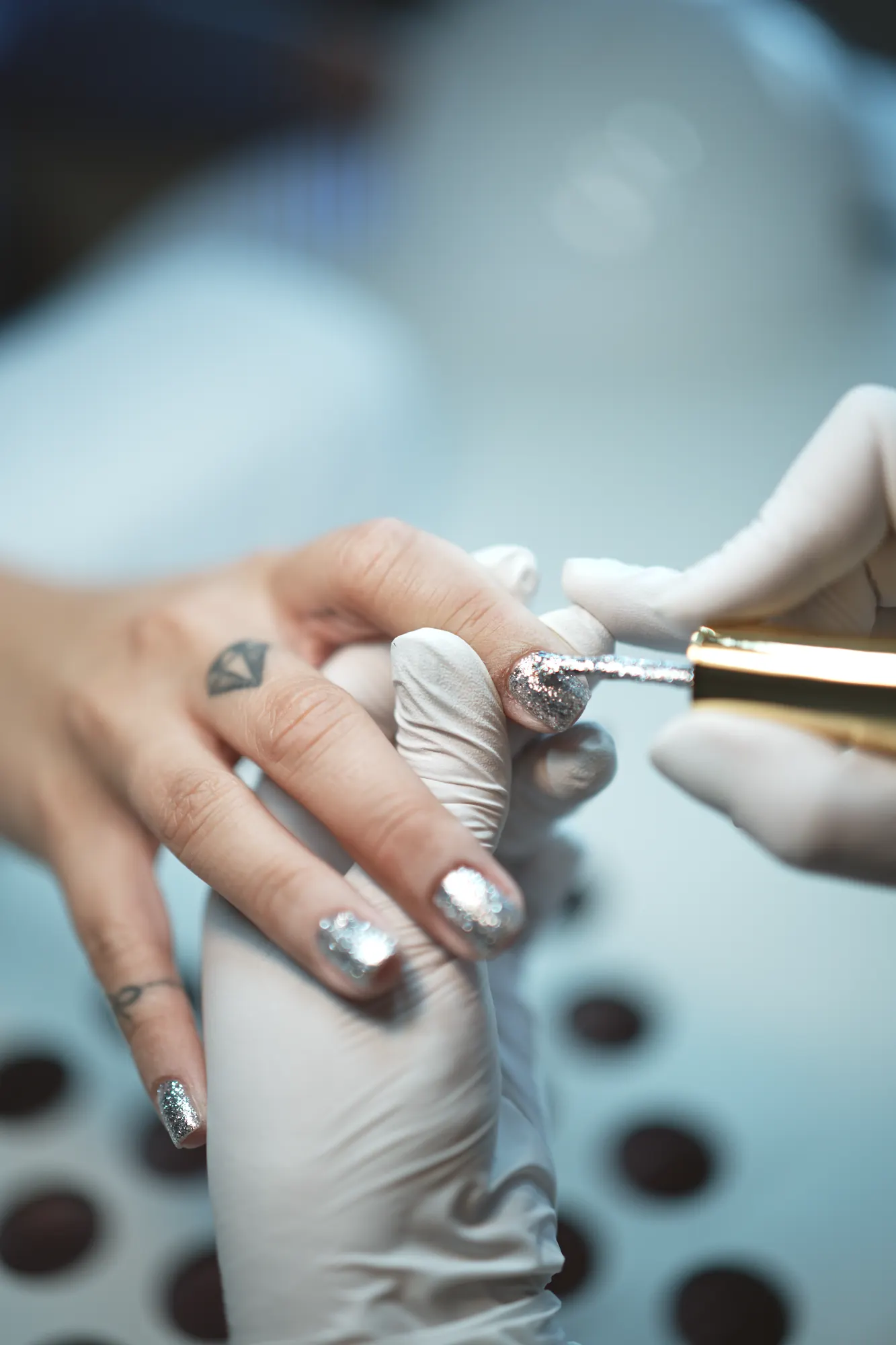 Behandschuhte Hände tragen silbernen Glitzer auf einen Nagel auf