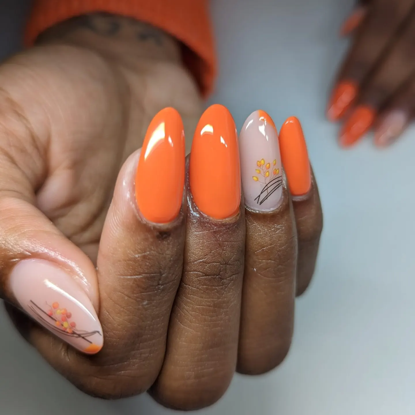 Mandelförmige Nägel in Orange, zwei in Nude mit Herbstzweigen und Beeren